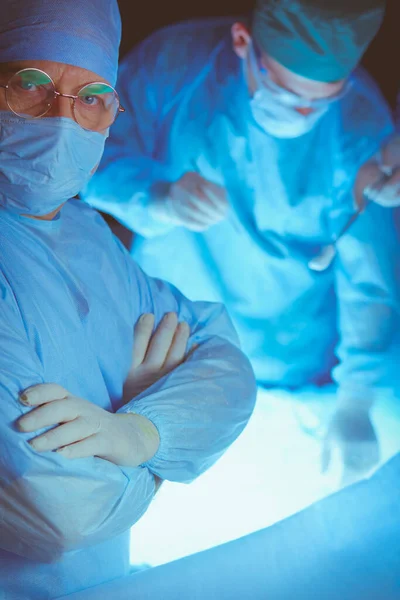 Grupo de cirujanos trabajando en quirófano tonificado en azul. Equipo médico realizando la operación — Foto de Stock