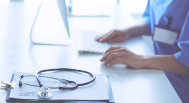 Kadın doktor masada oturuyor ve hastanede dizüstü bilgisayarla çalışıyor.