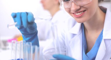 Kadın araştırmacı, beyaz arka planda izole edilmiş ilaç şişeleri ve mataralarla çevrili.