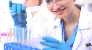 Kadın araştırmacı, beyaz arka planda izole edilmiş ilaç şişeleri ve mataralarla çevrili.