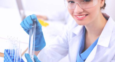 Kadın araştırmacı, beyaz arka planda izole edilmiş ilaç şişeleri ve mataralarla çevrili.