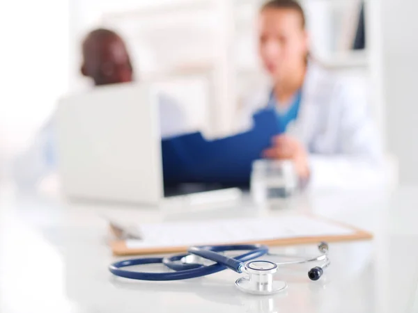 Estetoscópio na mesa e jovens médicos como pano de fundo — Fotografia de Stock