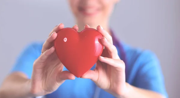 Jeune femme médecin tenant un cœur rouge, debout sur fond gris — Photo