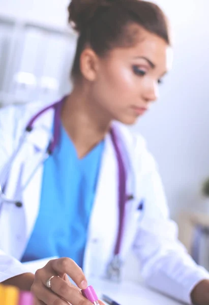 Hermosa joven sonriente doctora sentada en el escritorio y escribiendo. —  Fotos de Stock