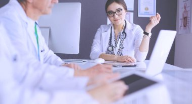 Ciddi bir tıbbi ekip parlak bir ofiste dizüstü bilgisayar kullanıyor.