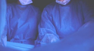 Ameliyathanede çalışan bir grup cerrah mavi tonda çalışıyor. Tıbbi ekip operasyon yapıyor.