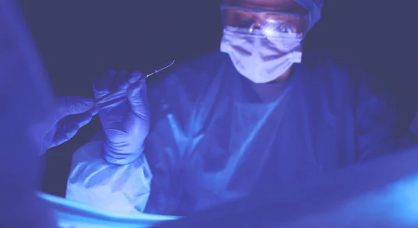 Medico che esegue un intervento chirurgico in uno sfondo scuro. — Foto Stock