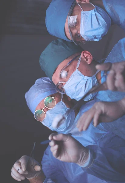 Grupo de cirurgiões no trabalho em sala de operações tonificada em azul. Equipe médica realizando operação — Fotografia de Stock