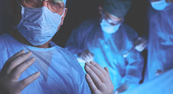 Grupo de cirurgiões no trabalho em sala de operações tonificada em azul. Equipe médica realizando operação — Fotografia de Stock