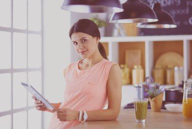 Mutfakta dijital tablet kullanan güzel genç bir kadın.