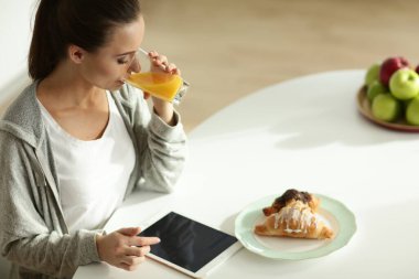 Mutfakta portakal suyu ve tableti olan genç bir kadın..