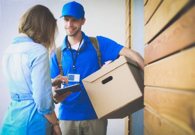 Mavi üniformalı gülümseyen kurye servis konseptine paket kutusu teslim eden teslimatçı.