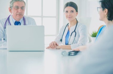 Ciddi bir tıbbi ekip, parlak bir danışma odasında dizüstü bilgisayar kullanıyor.