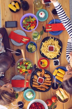 Ahşap masada otururken birlikte yemek yiyen bir grup insanın üst düzey görüntüsü. Masada yemek var. İnsanlar fast food yiyor..