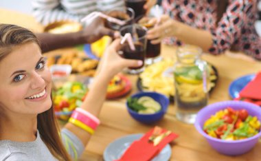 Ahşap masada otururken birlikte yemek yiyen bir grup insanın üst düzey görüntüsü. Masada yemek var. İnsanlar fast food yiyor. Bir kızın portresi.