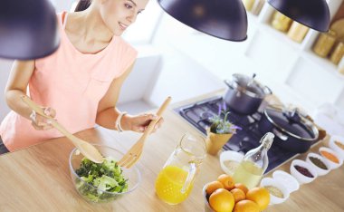 Gülümseyen genç kadın mutfakta taze salata karıştırıyor..