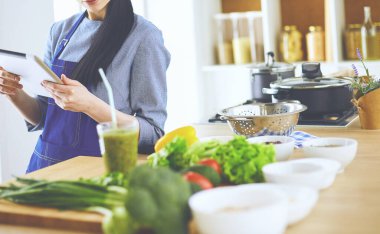 Mutfakta yemek yapmak için tablet bilgisayar kullanan genç bir kadın.