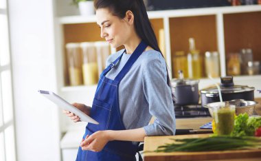 Mutfakta yemek yapmak için tablet bilgisayar kullanan genç bir kadın.