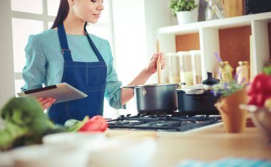Mutfakta yemek yapmak için tablet bilgisayar kullanan genç bir kadın.