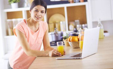 Mutfakta dizüstü bilgisayara benzeyen tariflerle gülümseyen genç bir kadın. Gıda blogcusu kavramı