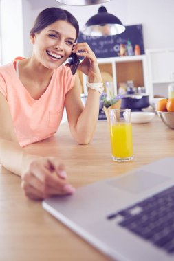 Mutfakta dizüstü bilgisayara benzeyen tariflerle gülümseyen genç bir kadın. Gıda blogcusu kavramı