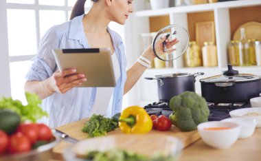 Mutfakta yemek yapmak için tablet bilgisayar kullanan genç bir kadın..