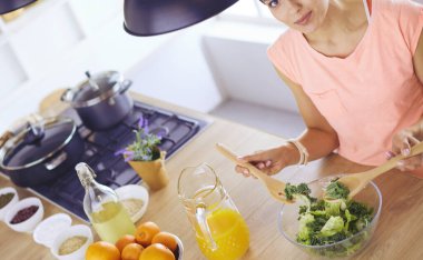 Gülümseyen genç kadın mutfakta taze salata karıştırıyor..