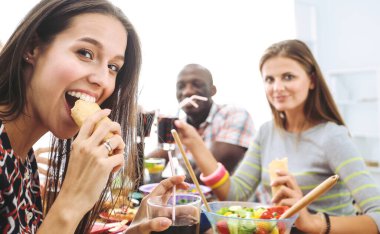 Ahşap masada otururken birlikte yemek yiyen bir grup insanın üst düzey görüntüsü. Masada yemek var. İnsanlar fast food yiyor..