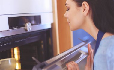 Güzel genç bayan pastasının fırında ne yaptığını kontrol ediyor.