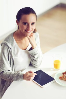 Mutfakta portakal suyu ve tableti olan genç bir kadın..