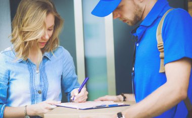 Mavi üniformalı gülümseyen kurye servis konseptine paket kutusu teslim eden teslimatçı.