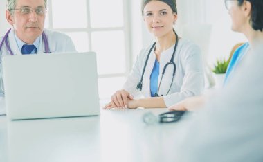 Ciddi bir tıbbi ekip, parlak bir danışma odasında dizüstü bilgisayar kullanıyor.