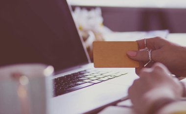 Kredi kartı tutan ve dizüstü bilgisayar kullanan genç bir kadın. Çevrimiçi alışveriş kavramı