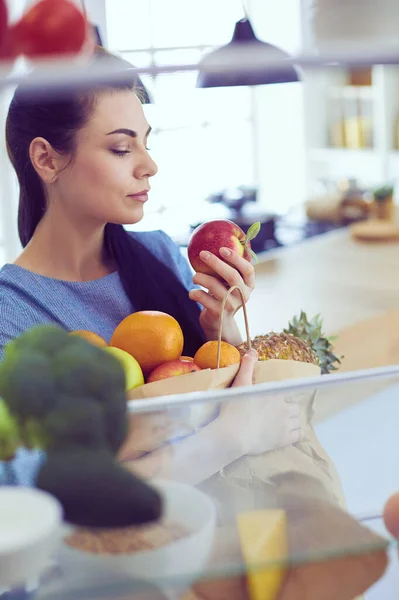 Smiling woman taking a fresh fruit out of the fridge, healthy food concept — Stock Photo, Image