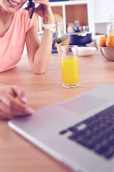 Mujer joven en la cocina con computadora portátil buscando recetas, sonriendo. Concepto de bloguero de alimentos — Foto de Stock