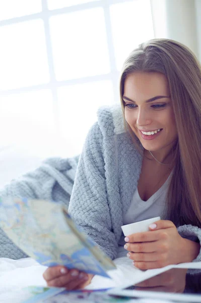 Mujer joven y relajada sentada en la cama con una taza de café y una tableta digital —  Fotos de Stock