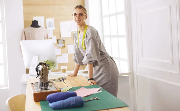 Het creëren van nieuwe modieuze stijlen. Vrolijke jonge vrouw naaien terwijl zitten op haar werkplek in mode workshop — Stockfoto