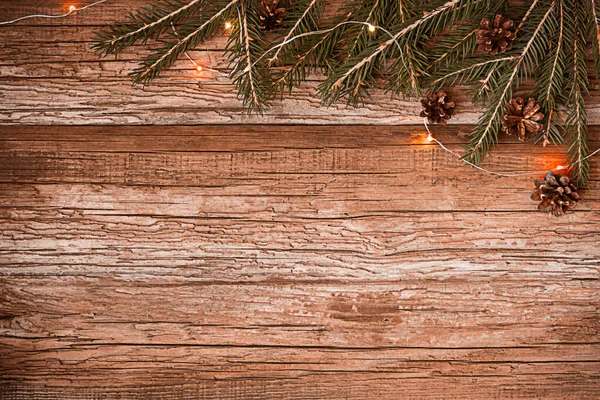 Christmas decoration with fir branches, cones and lights on wooden background. Flatly with copy space