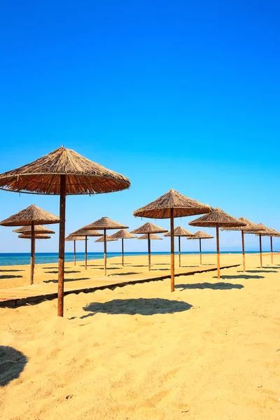 Row of wooden umbrellas at sandy beach, sea — Stock Photo, Image
