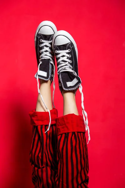 Female legs wearing striped pants and sneakers over red background. Funny woman legs