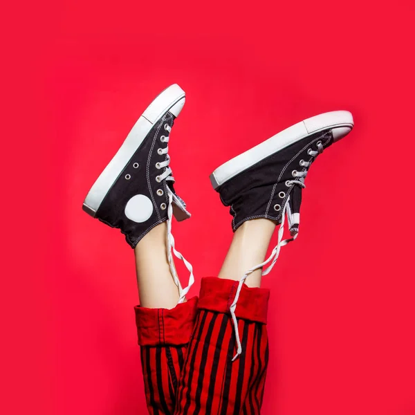 Patas Femeninas Con Pantalones Rayas Zapatillas Deporte Sobre Fondo Rojo — Foto de Stock