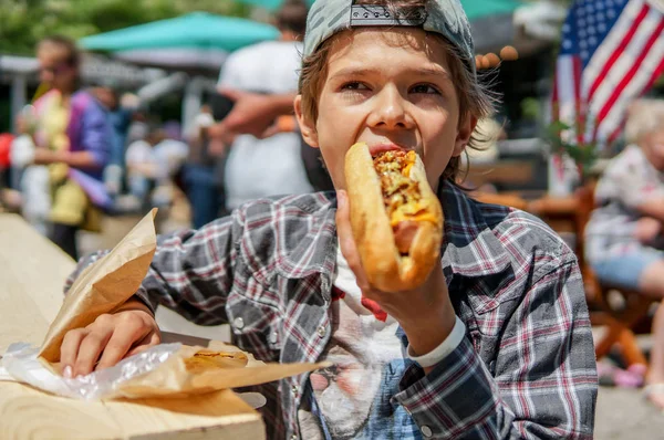 Boy eating barbecue grilled  hot dog on family picnic celebrating independence day with flag on the background