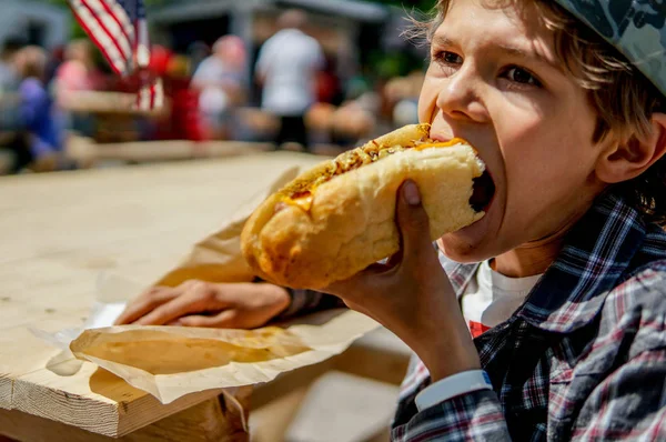 Boy eating barbecue grilled  hot dog on family picnic celebrating independence day with flag on the background