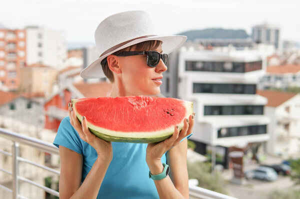 Portrait happy young woman is holding slice of watermelon over over city background