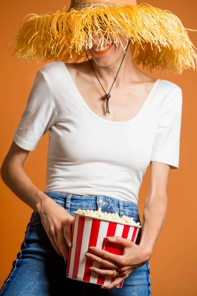 明るい背景上分離されたジーンズと帽子を着て食べるポップコーンを歓喜屈託のない素敵なかわいい女性の肖像画 — ストック写真