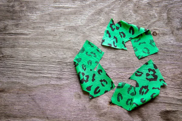 Recycling logo from green fabric over wooden background