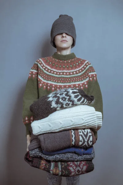 Young woman hold pile of sweaters wearing knitted hat and warm wool sweater, toned image