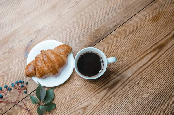 Good autumn morning with french croissant, coffee and autumn leaves over wooden rustic background