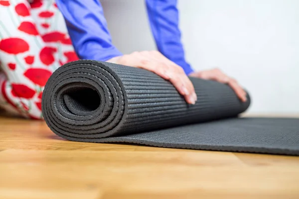 Time for meditation. Girl rolling fitness mat before, after class at home on wooden floor. Hands and legs close up, focus on mat