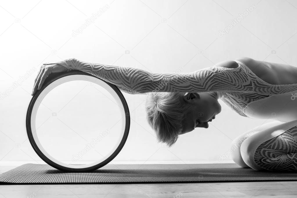 Portrait of gorgeous young woman practicing yoga indoor with a help of yoga wheel